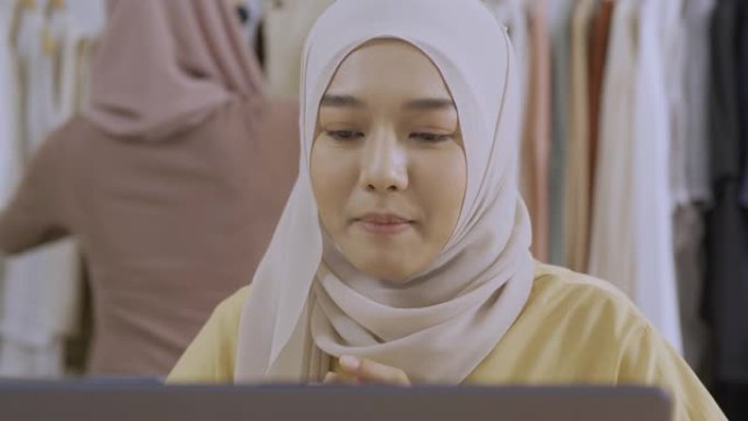 年轻美丽的亚洲女人正在她的服装店直播。她与顾客交谈并解释她的产品。