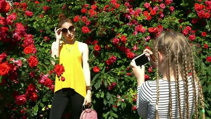 女孩在玫瑰园的智能手机上拍摄母亲的照片