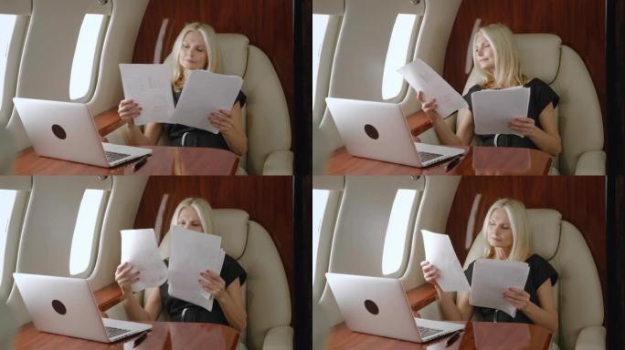 丰富的成熟女商人使用图表，商业论文和笔记本电脑，在私人飞机或头等舱飞机出差期间研究公司的增长战略