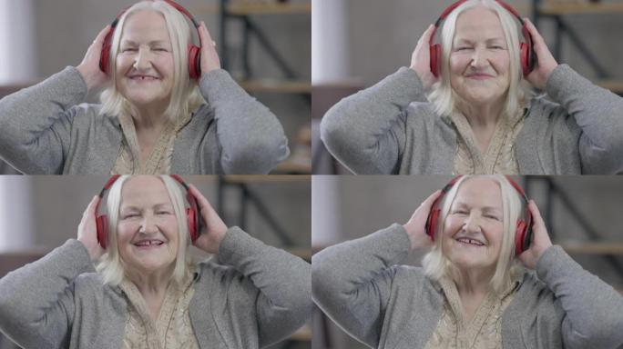欢快的微笑的白人退休人员的特写镜头，戴着耳机跳舞和唱歌，欣赏音乐。无忧无虑的轻松快乐的高级女人在室内