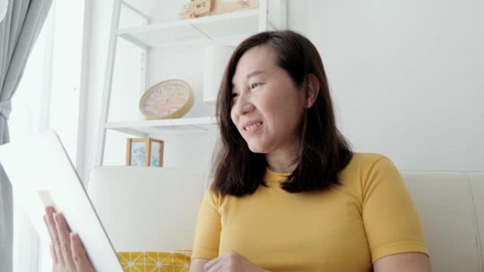 新型冠状病毒肺炎期间，亚洲成年女性坐在沙发上，在家附近的窗户上，用笔记本电脑进行视频会议，检疫生活方