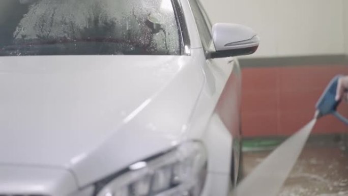 汽车清洁剂用高压水喷射清洗白色汽车。