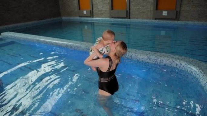 一个开朗的母亲和一个小孩在室内游泳池里玩耍。