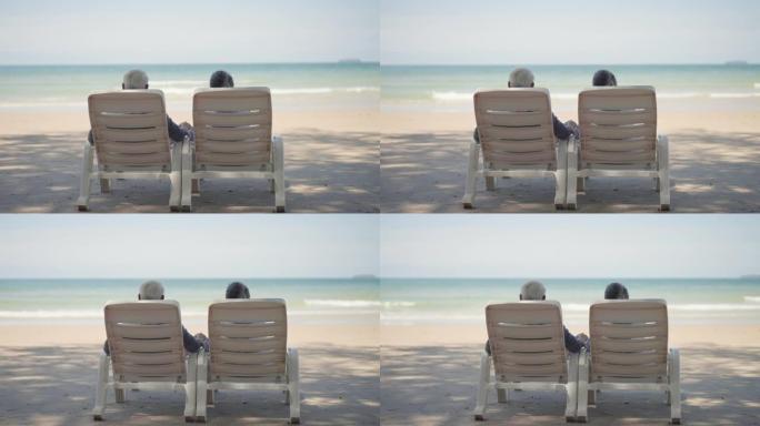 高级夫妇的手在海滩上休闲活动，高级妻子，高级丈夫在暑假那天在树荫下退休后，在沙滩椅子上牵着手放松。