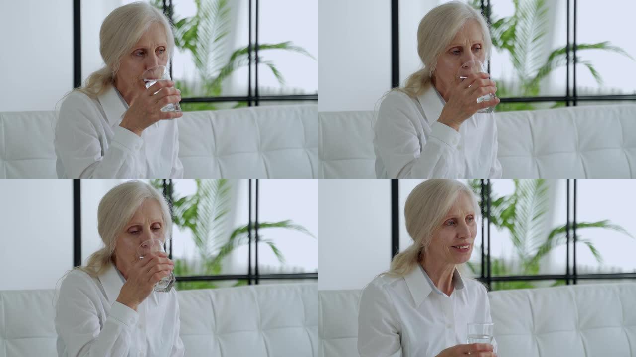 老年妇女坐在沙发上，用玻璃杯喝水