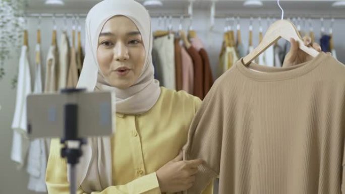 年轻美丽的亚洲女人正在她的服装店直播。她与顾客交谈并解释她的产品。