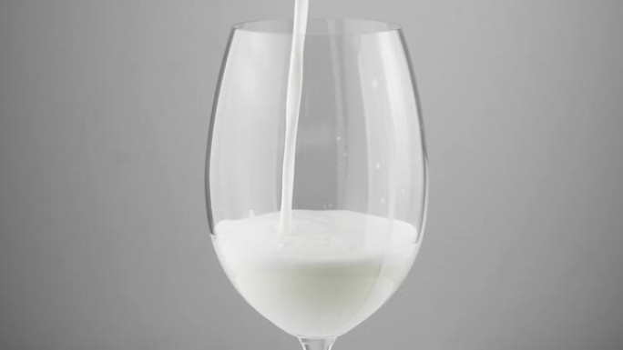 在灰色背景上倒入白色牛奶的玻璃杯。玻璃杯里的牛奶特写。