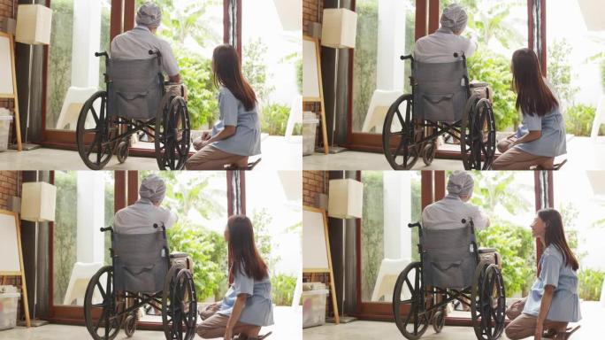老亚洲老人坐在家里的轮椅上，看着窗外思考。孤独的老人独自在家度过一天。家庭人寿保险的概念。