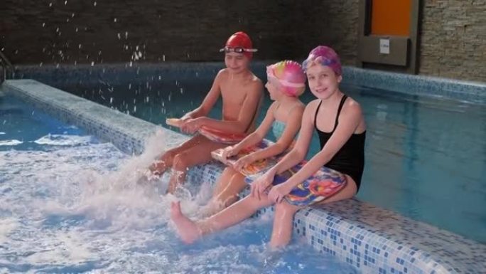 室内游泳池中戴游泳帽的三个小孩的肖像。