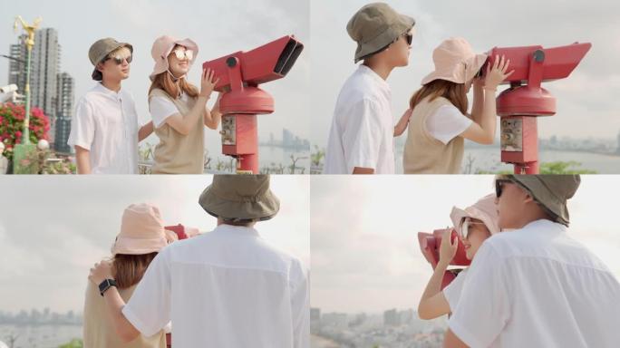 欢快的亚洲年轻夫妇游客在观看点使用投币式双筒望远镜观看城市背景。年轻人的关系。