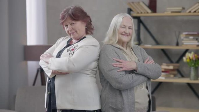 自信的白人女性双手交叉看着相机背靠背站在室内。积极快乐的女性退休人员在客厅摆姿势的肖像。自信和衰老