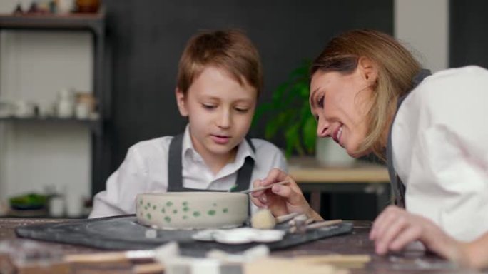 母亲在工作室协助儿子画碗。陶艺班作坊。妈妈和孩子花时间在一起做创造性的工作。慢动作