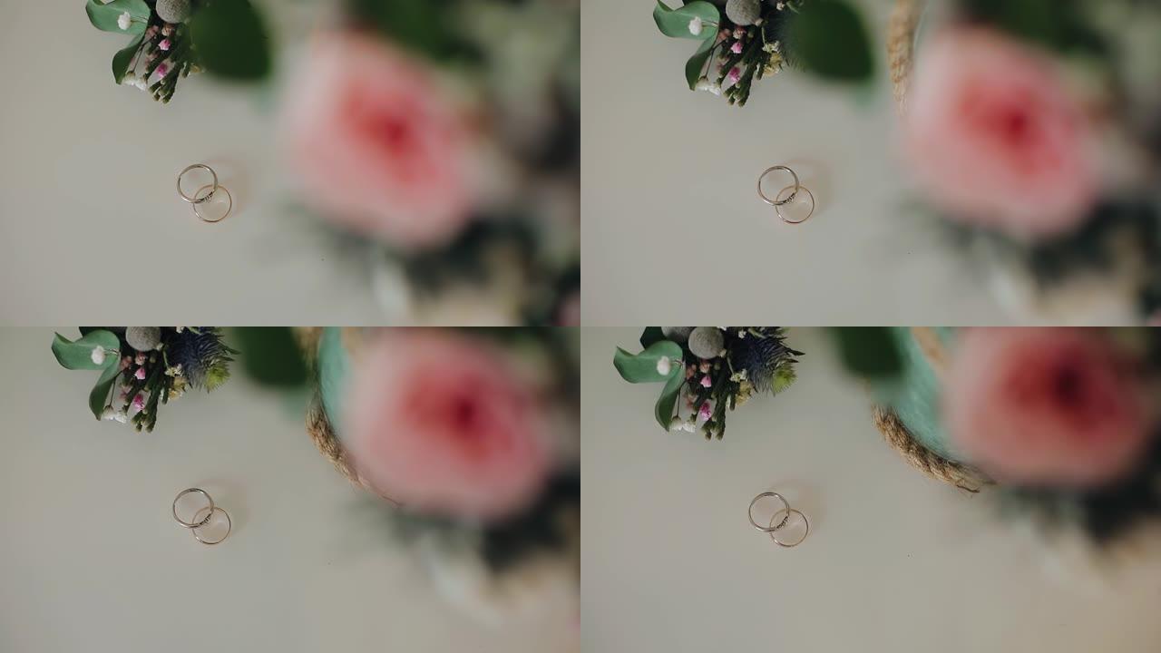 金色的结婚戒指躺在一束鲜花旁边的玻璃桌上。从上方拍摄特写