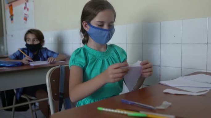 女学生在教室里折叠纸。新型冠状病毒肺炎概念
