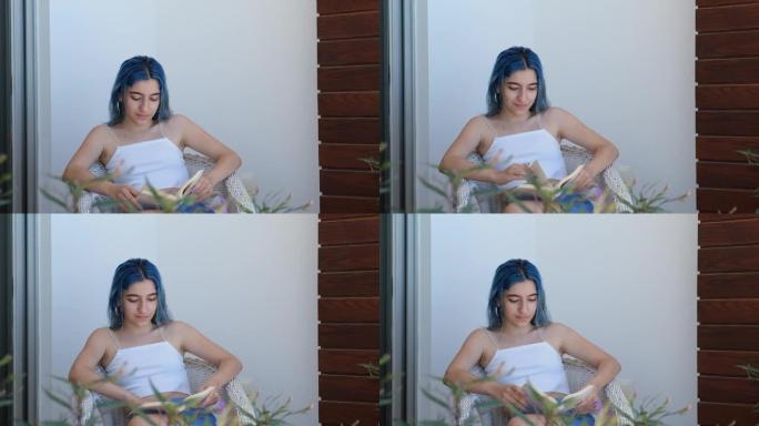 年轻现代的蓝色头发的女人在阳台上看书