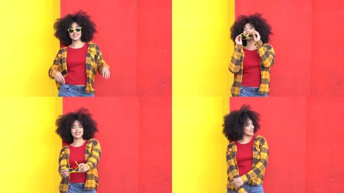 4k视频美丽的非洲裔美国女人，有着非洲的头发和五颜六色的衣服，在五颜六色的墙上微笑和姿势