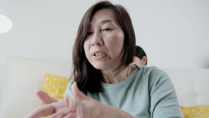 亚洲母亲视频电话给医生和按摩自己在新型冠状病毒肺炎期间在家疼痛和疼痛，检疫的生活方式概念。