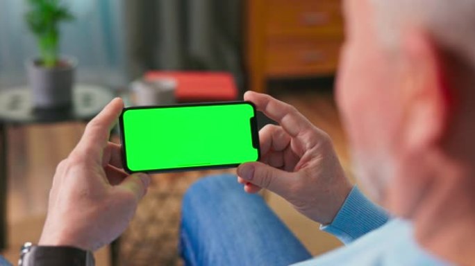 家里的老人在沙发上休息，使用水平横向纵向模式下的绿色模拟屏幕智能手机。女人使用平板电脑设备，浏览互联