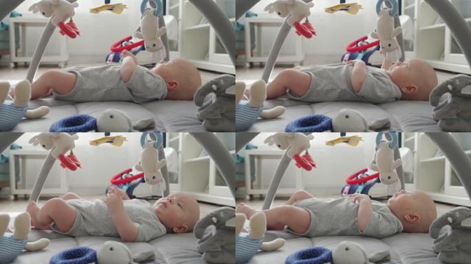 婴儿躺在带悬挂玩具的软游戏垫上，可爱的男婴在活动健身房玩伴上玩有趣的动物，客厅地板上2个月大的新生婴