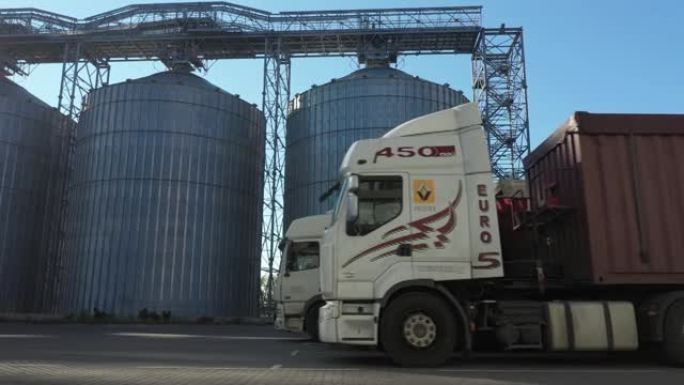 许多带有装满谷物的拖车的卡车的侧视图在带有仓库的电梯上等待卸货