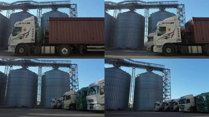 许多带有装满谷物的拖车的卡车的侧视图在带有仓库的电梯上等待卸货