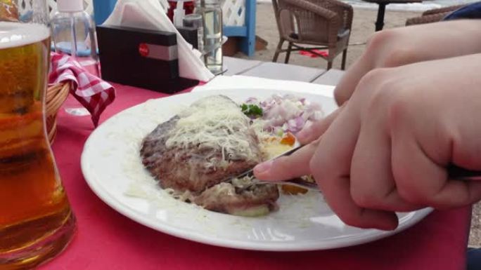 人在咖啡馆用叉子和刀子切掉一块油炸肉末，特写。巴尔干美食的国家烤盘-pljeskavica。餐厅里有