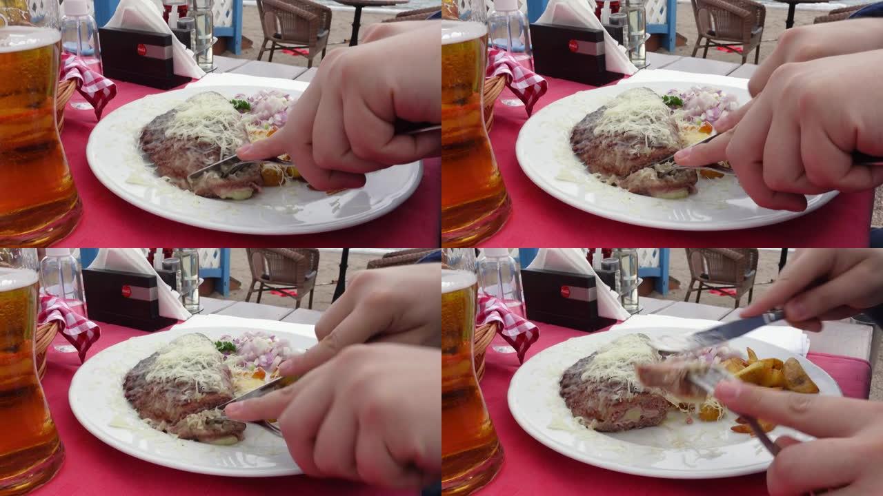 人在咖啡馆用叉子和刀子切掉一块油炸肉末，特写。巴尔干美食的国家烤盘-pljeskavica。餐厅里有