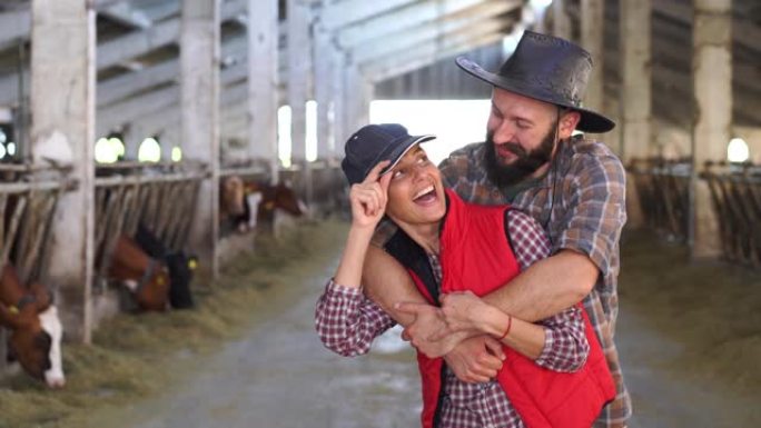在大型奶牛农场，穿着休闲服装的白人农民夫妇拥抱并微笑着对着镜头的4k视图。