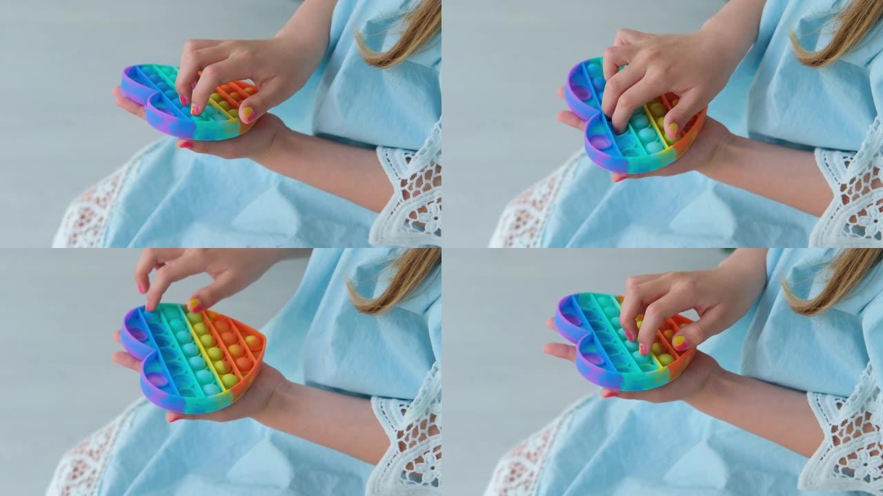 孩子玩彩虹流行它烦躁玩具。推气泡烦躁感官玩具-可清洗和可重复使用的硅应力缓解玩具。一个小女孩玩抗压玩