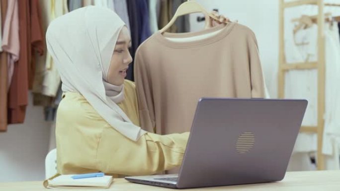 年轻美丽的亚洲女人正在她的服装店直播。她与顾客交谈并解释她的产品。