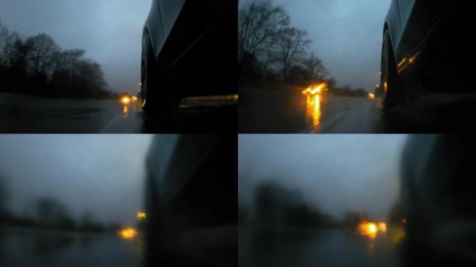 详细说明汽车后轮在潮湿的道路上在大雨中行驶。雨水溅到相机上
