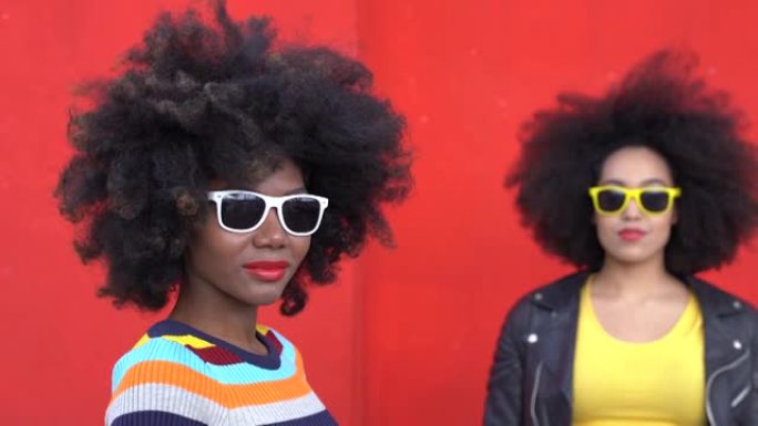 4k视频美丽的非洲模特，非洲头发和五颜六色的衣服在红墙上微笑和摆姿势