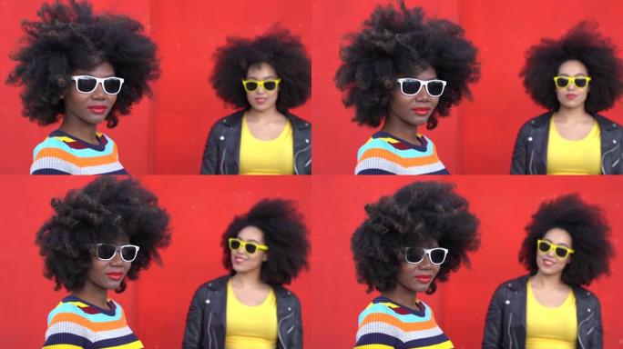 4k视频美丽的非洲模特，非洲头发和五颜六色的衣服在红墙上微笑和摆姿势