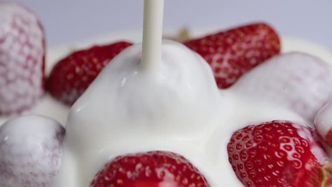 将奶油或酸奶倒在多汁的新鲜草莓上。覆盖着白色乳白色液体的甜红色浆果。维生素健康甜点，健康食品。特写。
