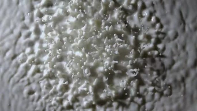 强烈的振动使白色牛奶的下降上升。快速变化的振动波结构会产生共振，球形液滴悬浮在乳液的表面上。慢动作。