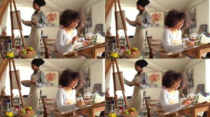 4k视频两名漂亮的美国黑人年轻女性在工作室里画画，看着画，微笑着