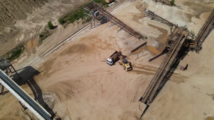轮式装载机将沙子装载到自卸车中。露天矿附近建筑砂生产的鸟瞰图