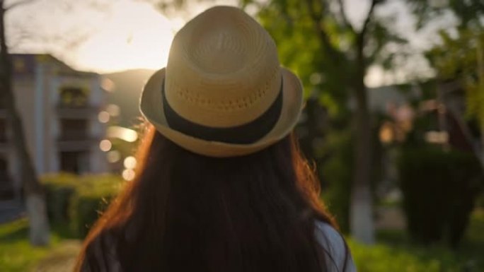 夏天。戴草帽的女人，向前走。后视图。背景中的日落。多莉开枪