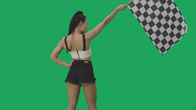 黑发挥舞着黑白方格赛车标志的后视图，标志着比赛开始。年轻女子在绿屏背景下摆姿势特写。慢动作就绪，4k