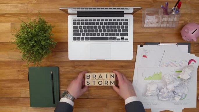 短语头脑风暴是由双手放在办公室桌子上的木制立方体组成的。术语头脑风暴是由桌面上的木制立方体制成的。概