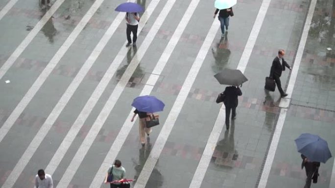 一群面目全非的人在雨中戴着五颜六色的雨伞走在车站广场上。慢动作。雨季。