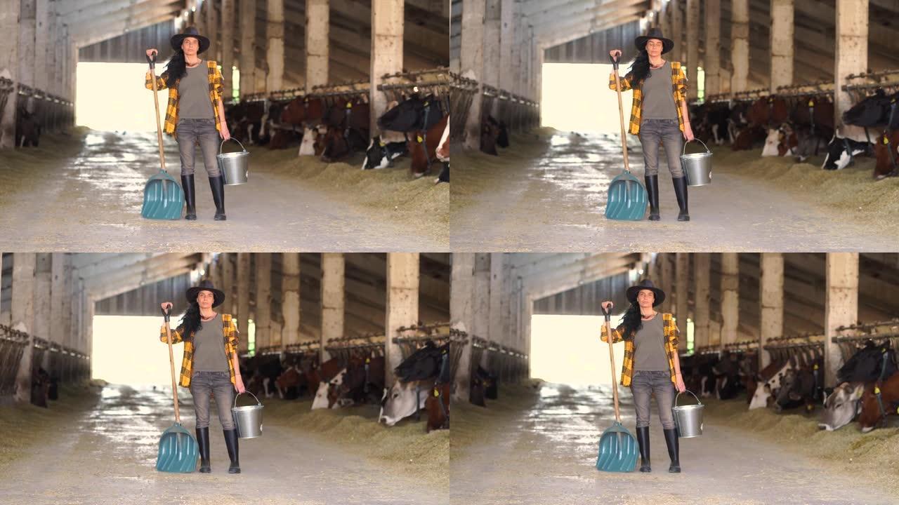4k视频中年女农场工人，戴着牛仔帽，拿着水桶和铲子，看着奶牛场里的摄像机，担心而严肃