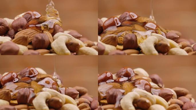 金色蜂蜜的涓涓细流从一堆坚果中缓慢流动。蜂蜜滴落并包裹杏仁，腰果和榛子的混合物。关闭甜糖浆中的坚果的