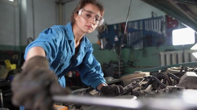 修理车间的发动机。一位年轻的汽车修理工手里拿着一把大扳手，拧开了什么东西。车间工作。妇女的平等权利。