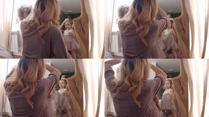 年轻的妈妈在家里的镜子里为小女儿做发型