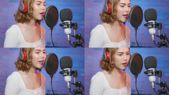 年轻的微笑女歌手戴着带麦克风的耳机，在五颜六色的音乐工作室里录制歌曲。