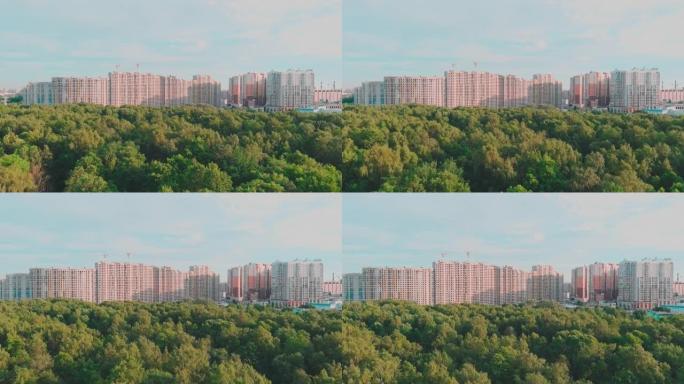 无人机飞越公园，驶向日落时正在建设的巨大住宅区，建筑起重机，绿树，圣彼得堡，俄罗斯