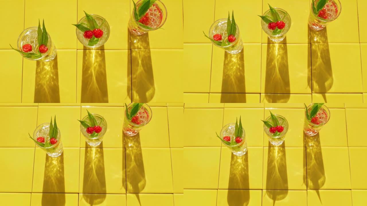 清爽的夏季饮料在水晶眼镜与绿叶覆盆子黄色瓷砖背景阴影。甜冷天然鸡尾酒炎热的夏日。苏打水水果浆果薄荷滋