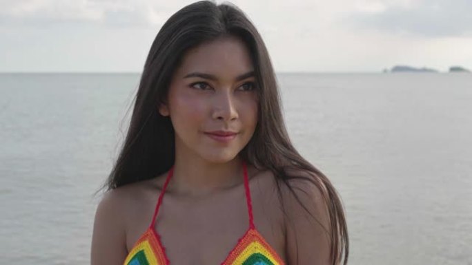 穿着比基尼的年轻亚洲美女在镜头前看起来很性感。夏天天气下，热带海滩上的头发随风吹来。旅行和生活方式概