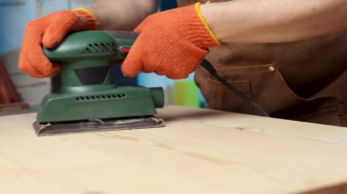 木匠用电动砂光机打磨木板的特写。木匠用砂光机研磨木材